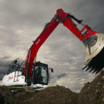 An excavator on a mound of dirt, ready to scoop up a load of dirt.